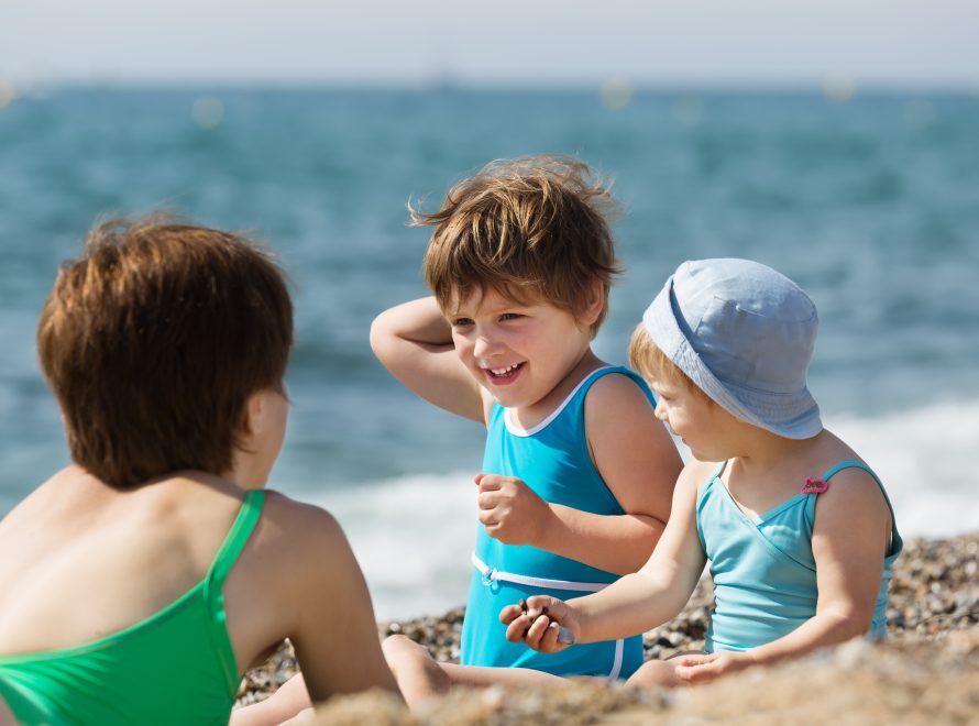 Niños pequeños jugando en la playa durante las vacaciones de verano para ilustrar consejos de salud infantil.